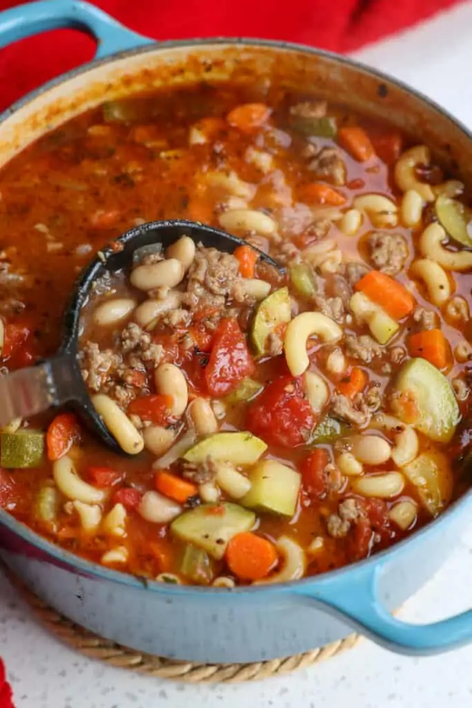 A ladle full of tasty soup with Italian Sausage, onion celery, carrots, zucchini, tomatoes, beans, and pasta. 
