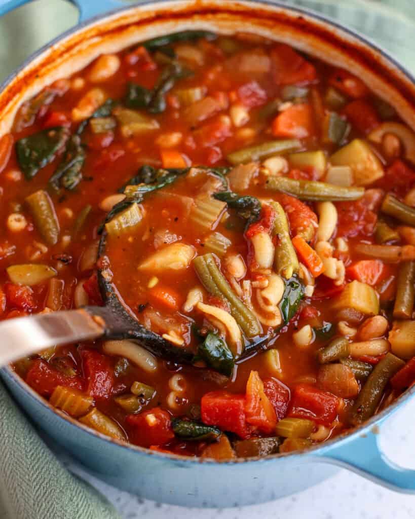 A Dutch oven and ladle full of minestrone soup.