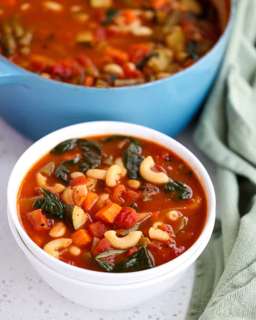 A single serving white bowl full of minestrone soup.