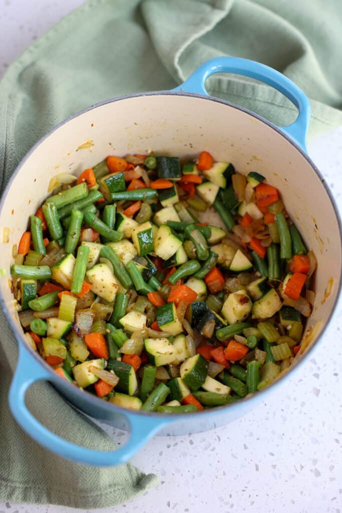 Start by cooking the onions , celery, carrots, green beans, and zucchini. 