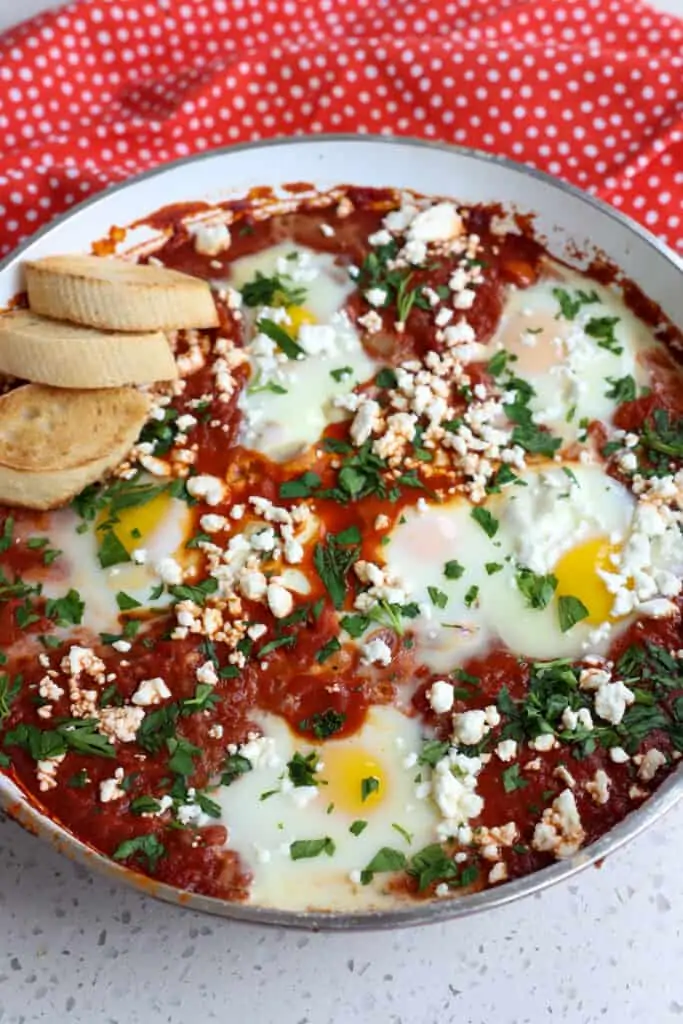 A skillet full of shakshuka topped with feta cheese and chopped fresh parsley. 