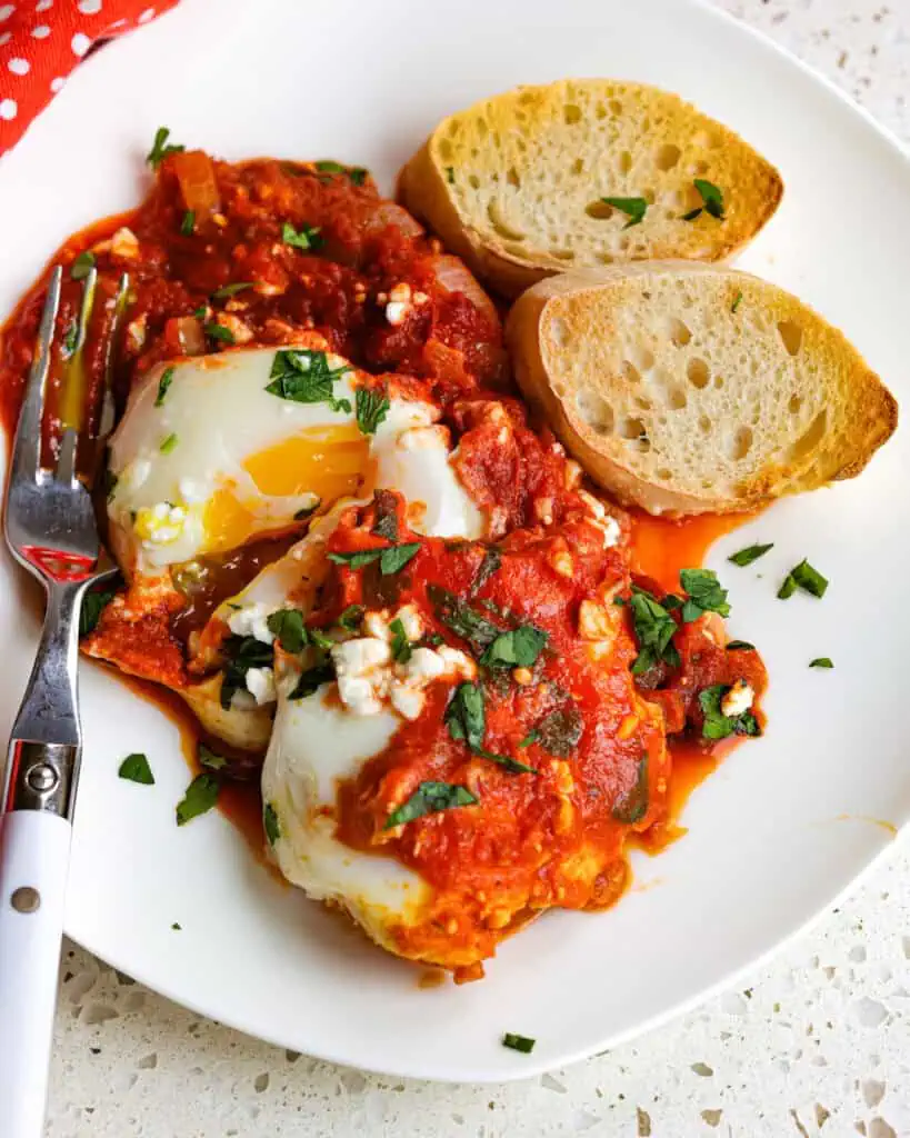 A plate full of gently poached eggs simmered in onions, peppers, garlic, and crushed tomatoes with spices. 