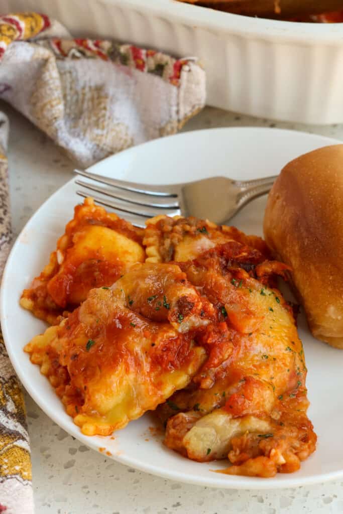 Baked Ravioli casserole on a plate with a roll. 