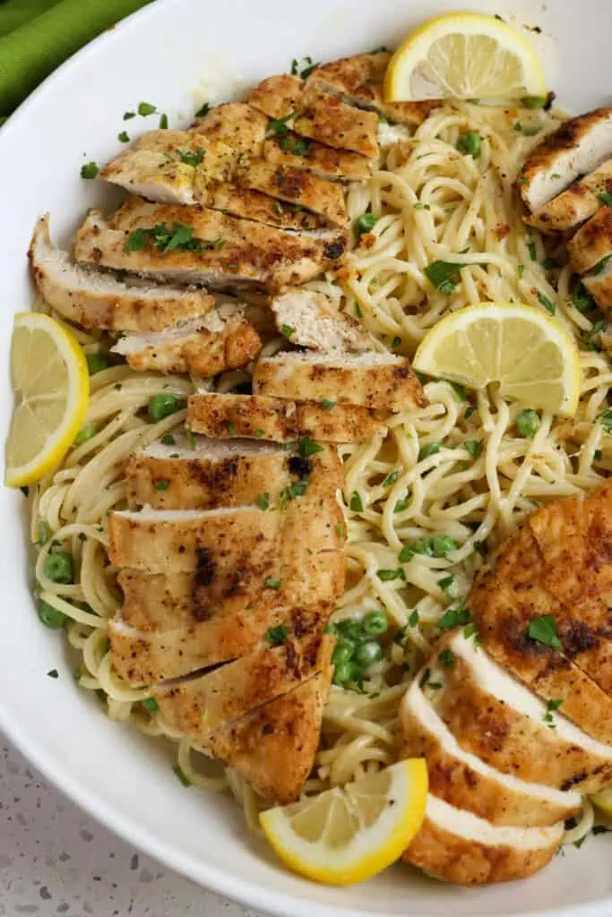 A large bowl full of spaghetti in a creamy lemon sauce and topped with sliced lemon pepper chicken. 