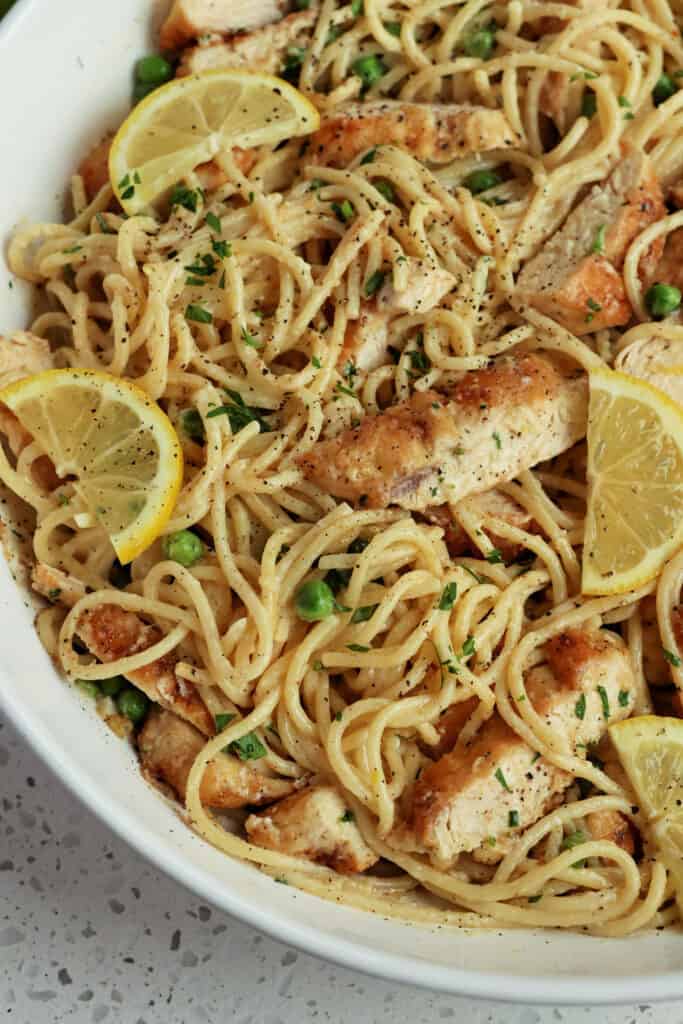 A large bowl of lemon chicken pasta garnished with fresh lemon and chopped parsley. 