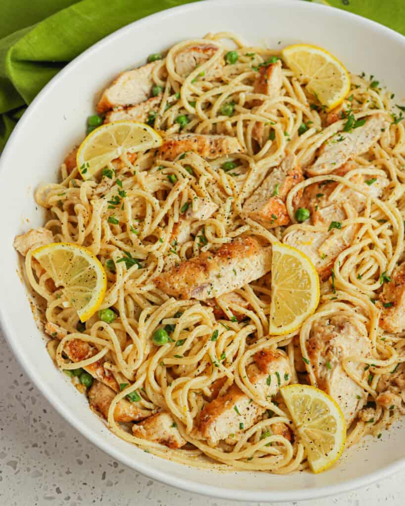 A white serving bowl full of lemon chivcken pasta. 