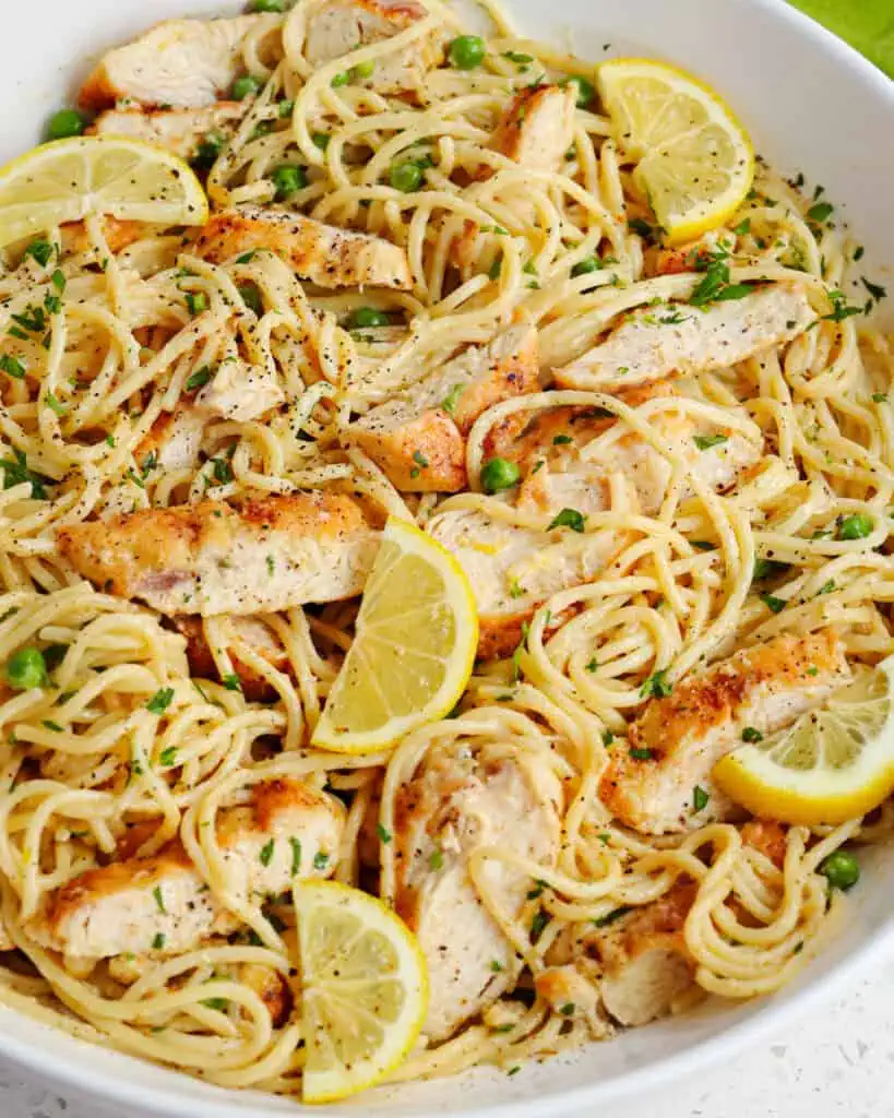 A large bowl full of spaghetti in a creamy lemon sauce and topped with sliced lemon pepper chicken.