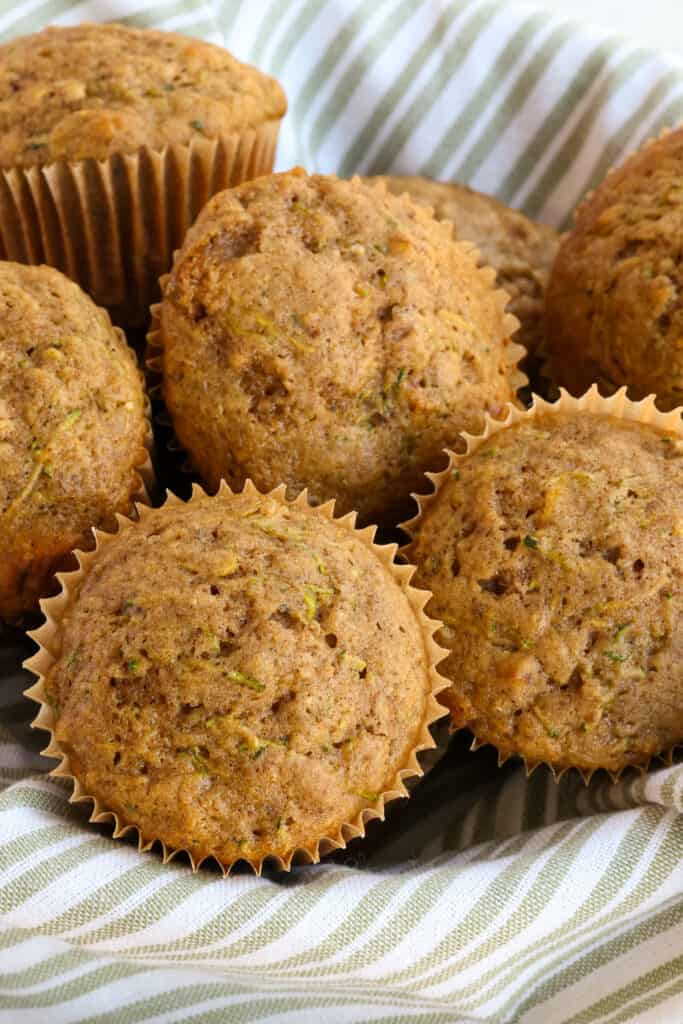 A basket full of zucchini muffins with fresh zucchini and chopped pecans. 