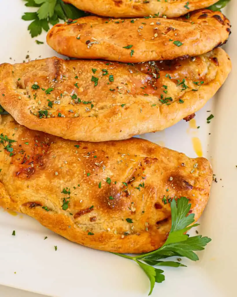 Multiple calzone on a plate with a few sprigs of Italian parsley.