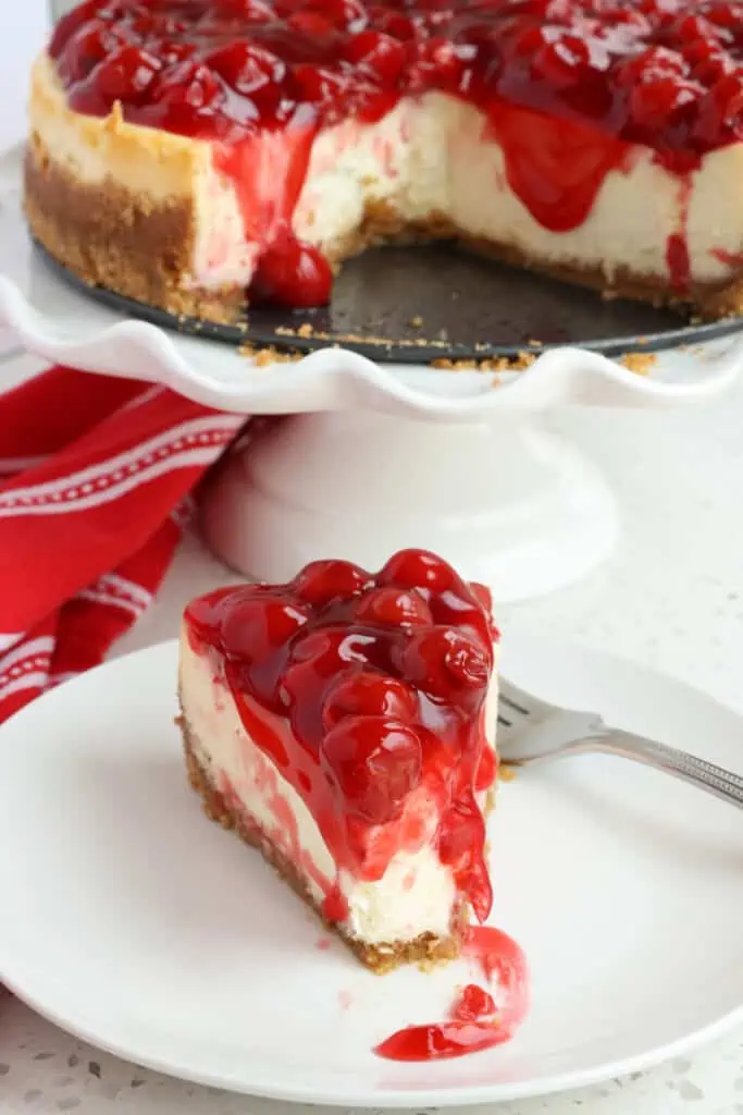 A slice of cherry cheesecake with a bite removed on a plate.  