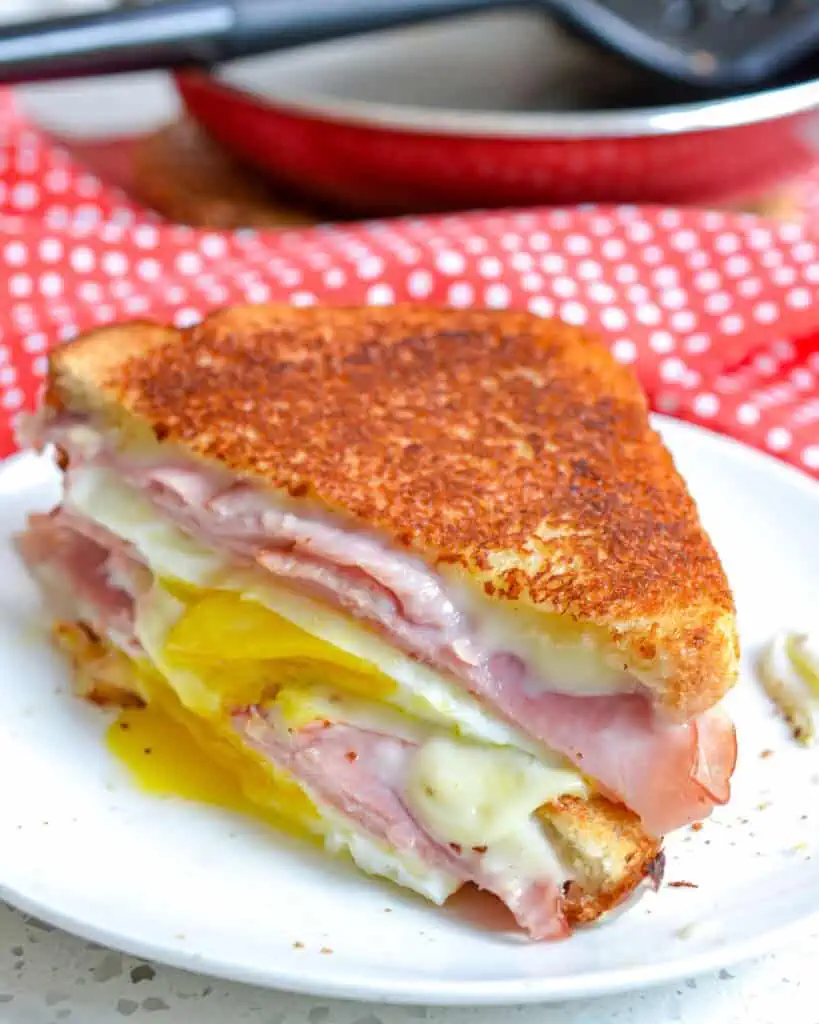 A double stacked egg sandwich on a plate with a skillet and spatula in the background.
