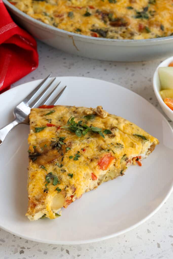 A slice of frittata on a plate with fresh fruit. 