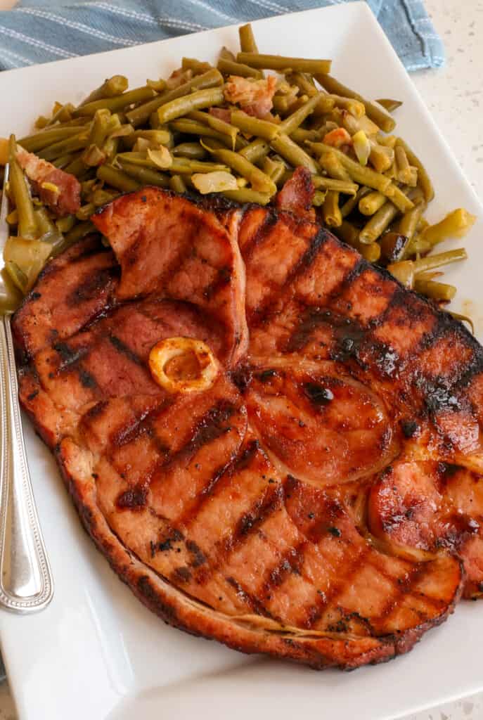Ham Steak Recipe A full ham steak on a platter with southern green beans.