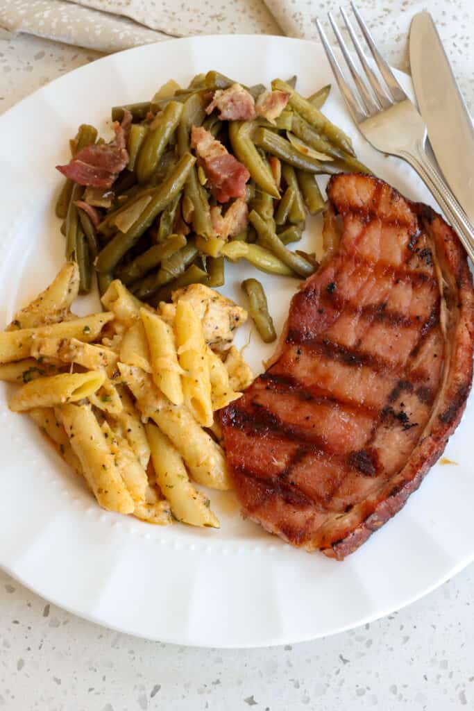 Ham Steak Ham steak with mac and cheese, and southern green beans on a serving plate.