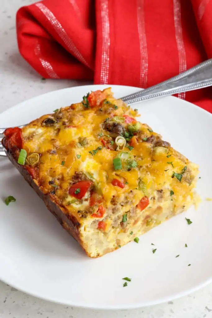 A slice of cheesy breakfast casserole with sausage, onions, and peppers.  