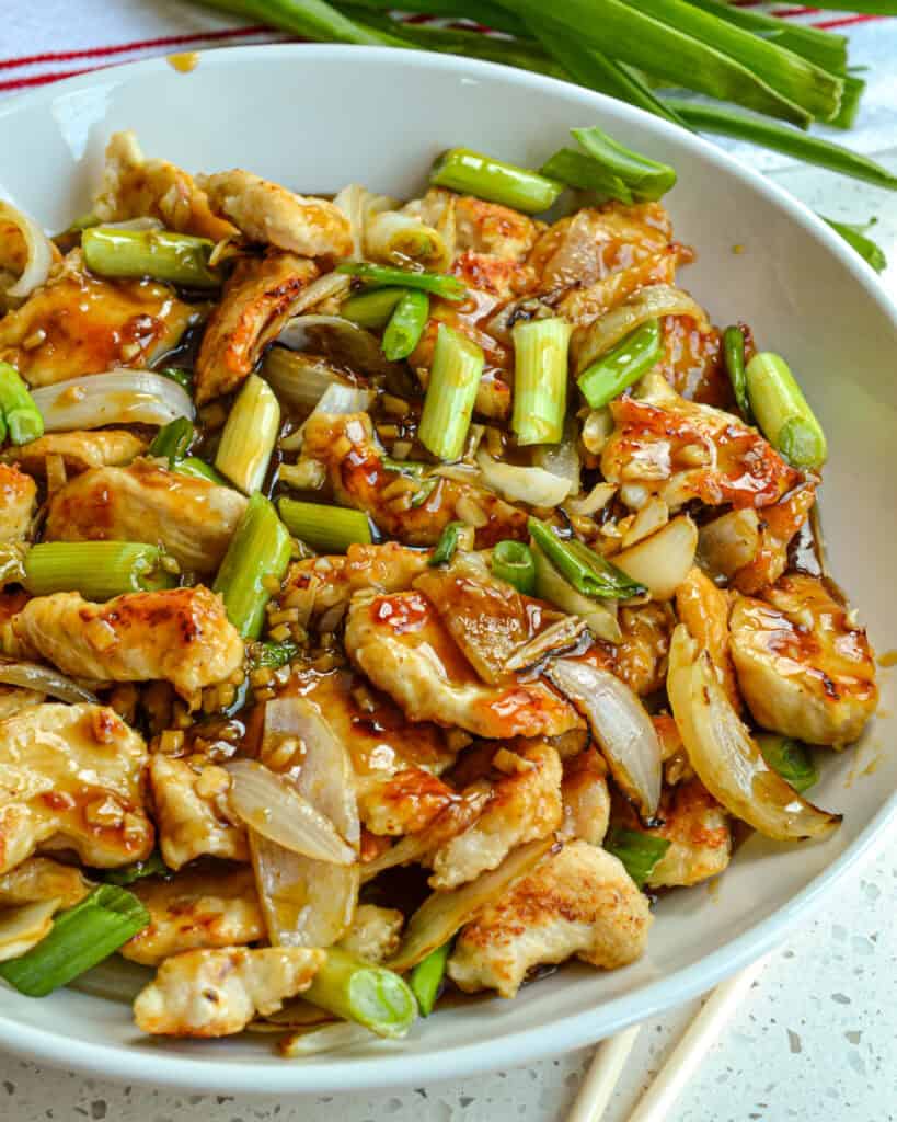 A close up view of Mongolian chicken in a white serving bowl. 