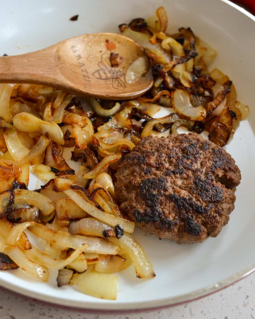 Grilled onions and burger patties in a skillet.  