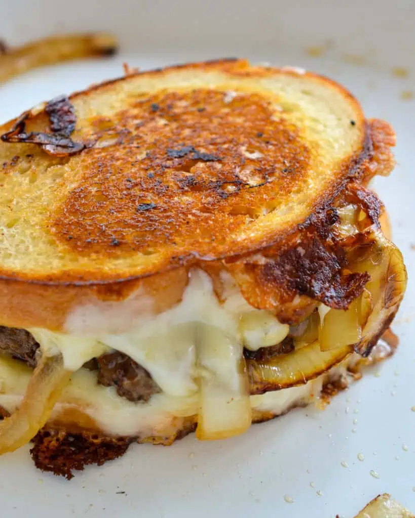 A close up view of a patty melt with onions and cheese in a skillet. 