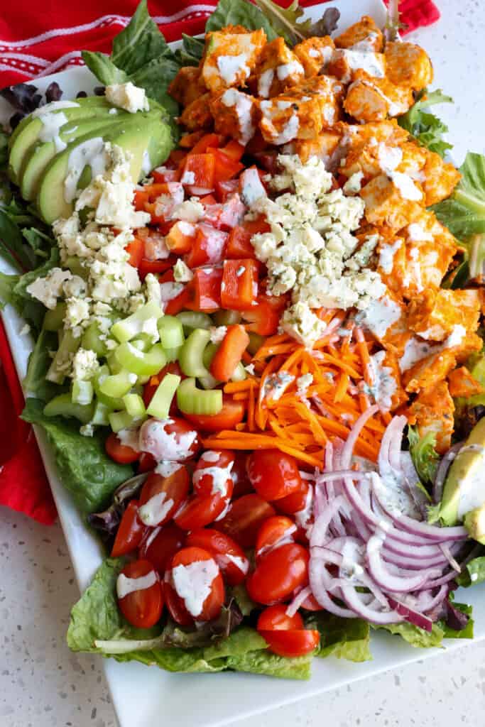 A platter full of Buffalo Chicken Salad with celery, carrots, blue cheese, red onions, and tomatoes. 