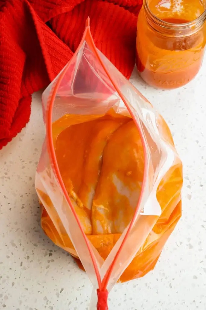 Chicken marinating in buffalo sauce in a zipper bag. 