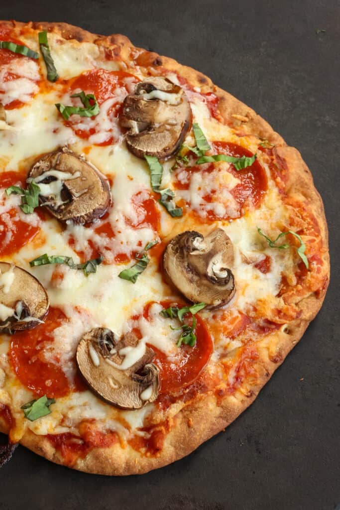 Fresh baked naan pizza bread with pepperoni, mushrooms, mozzarella, and basil.