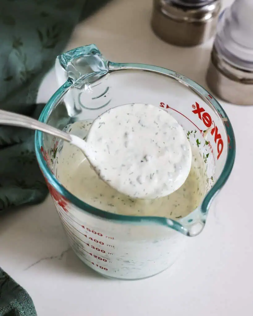A glass measuring cup and a ladle full of ranch dressing.