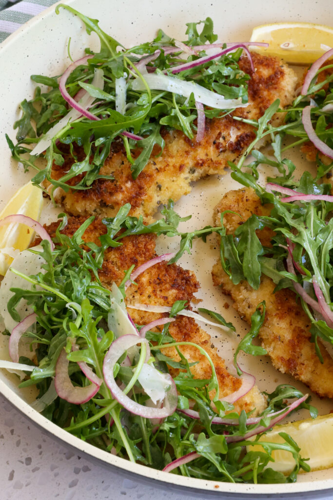 Quick, easy, and elegant Chicken Milanese combines crisp breaded pan fried chicken breasts with a simple arugula and red onion salad 