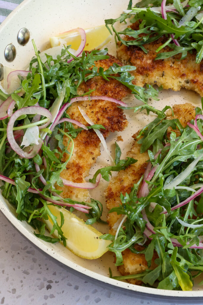Chicken Milanese combines crisp breaded pan fried chicken breasts with a simple arugula and red onion salad tossed with a simple lemon dressing and topped with Parmesan shavings.