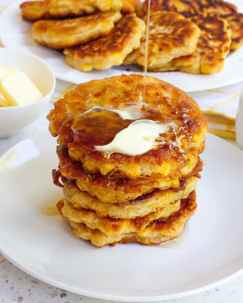 A plate full of corn fritters with butter and syrup on them.