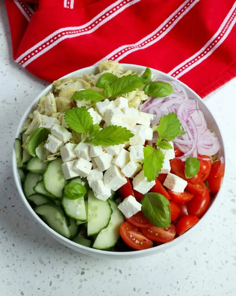 Once the orzo pasta cools add it to a large bowl with cucumbers, grape tomatoes, artichoke hearts, red onion, and feta cheese.
