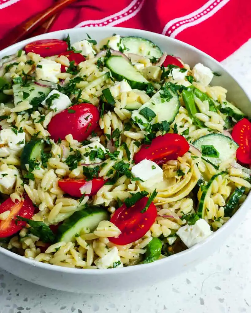 A close up view of orzo pasta salad in a large white serving bowl. 