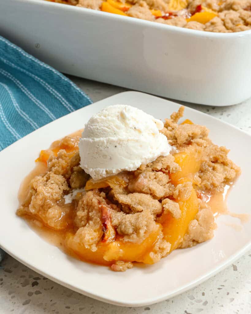 Peach cobbler with a scoop of vanilla ice cream on a single serving white plate. 
