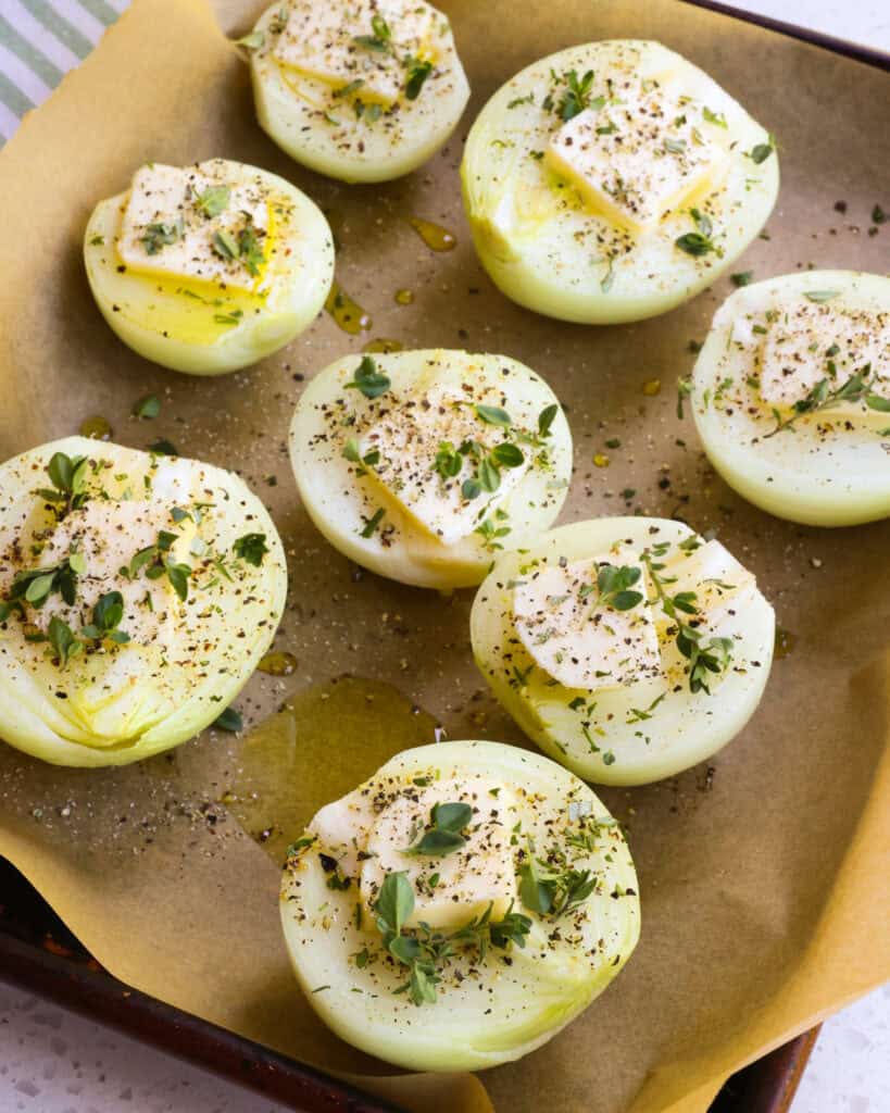 Halved onions with butter and herbs on a parchment covered baking sheet. 