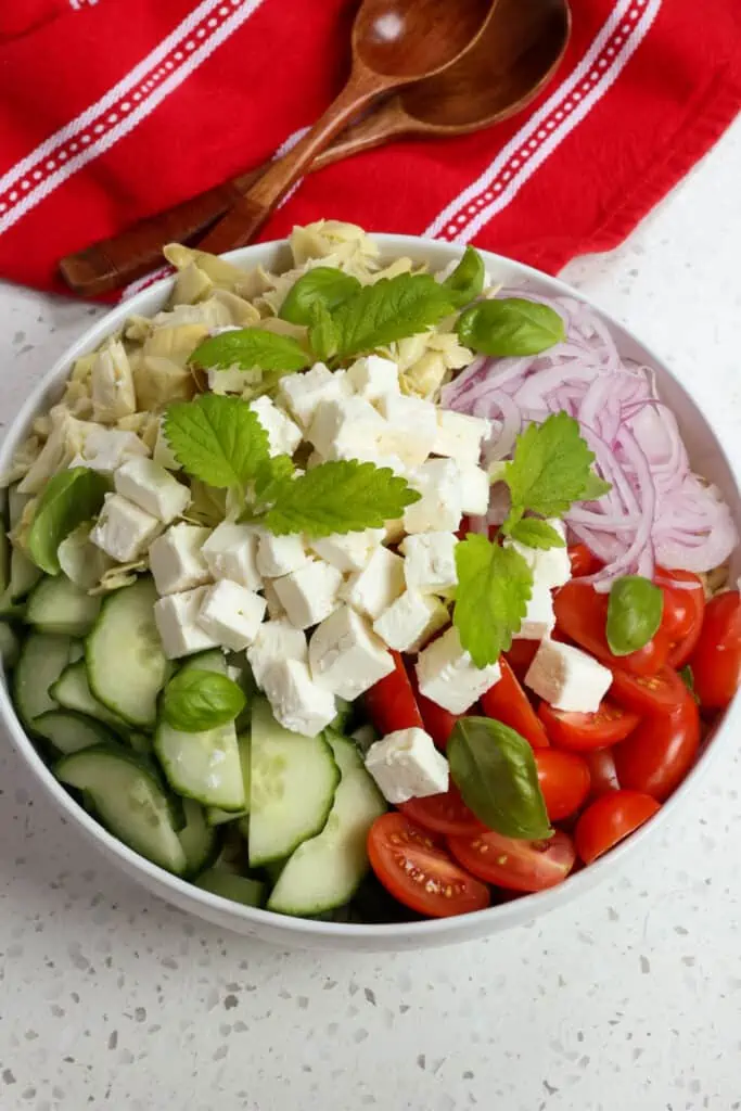 Once the orzo pasta cools add it to a large bowl with cucumbers, grape tomatoes, artichoke hearts, red onion, and feta cheese.