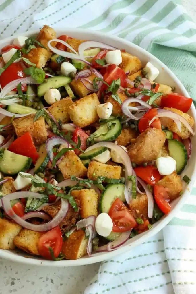 Easy Summer Panzanella Salad with toasted Italian bread cubes, tomatoes, cucumbers, red onions, mozzarella pearls, capers, and fresh basil all tossed in a simple oil and vinegar dressing.