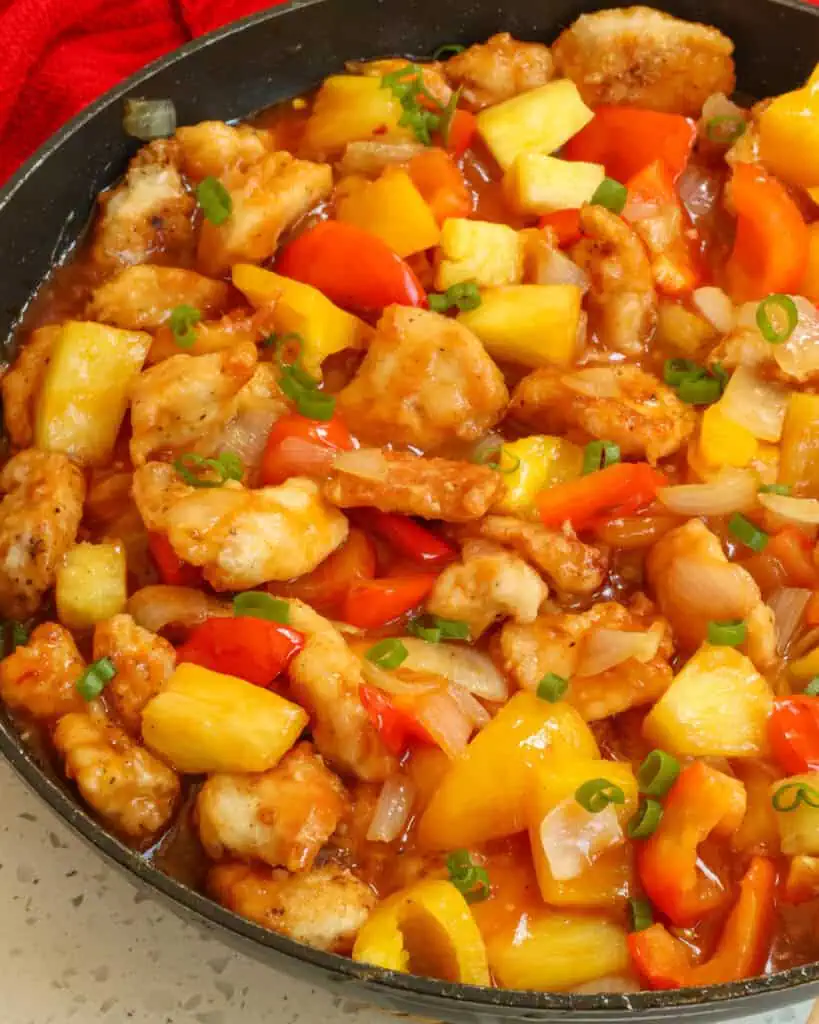A close up view of pineapple chicken with fresh pineapple, orange and red bell peppers, onions, and garlic all in a lightly sweetened pineapple sauce.