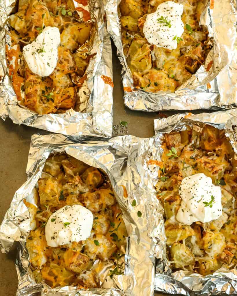 Four foil packets topped with cheese, fresh herbs, and sour cream on top of a baking sheet.