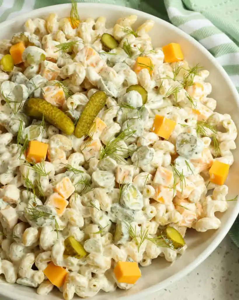Eine Servierschüssel voller Dillgurken-Nudelsalat mit kleinen Cheddar-Würfeln und gehackten Dillgurken.