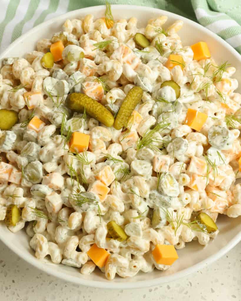 Overhead view of dill pickle pasta salad garnished with chopped fresh dill and sliced baby dill pickles. 