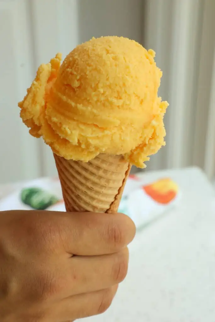 A scoop of orange sherbet on a sugar cone. 