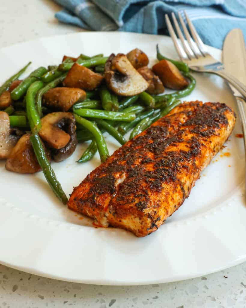 Blackened Mahi Mahi on a serving plate with green beans and mushrooms and a fork and a knife on the plate.