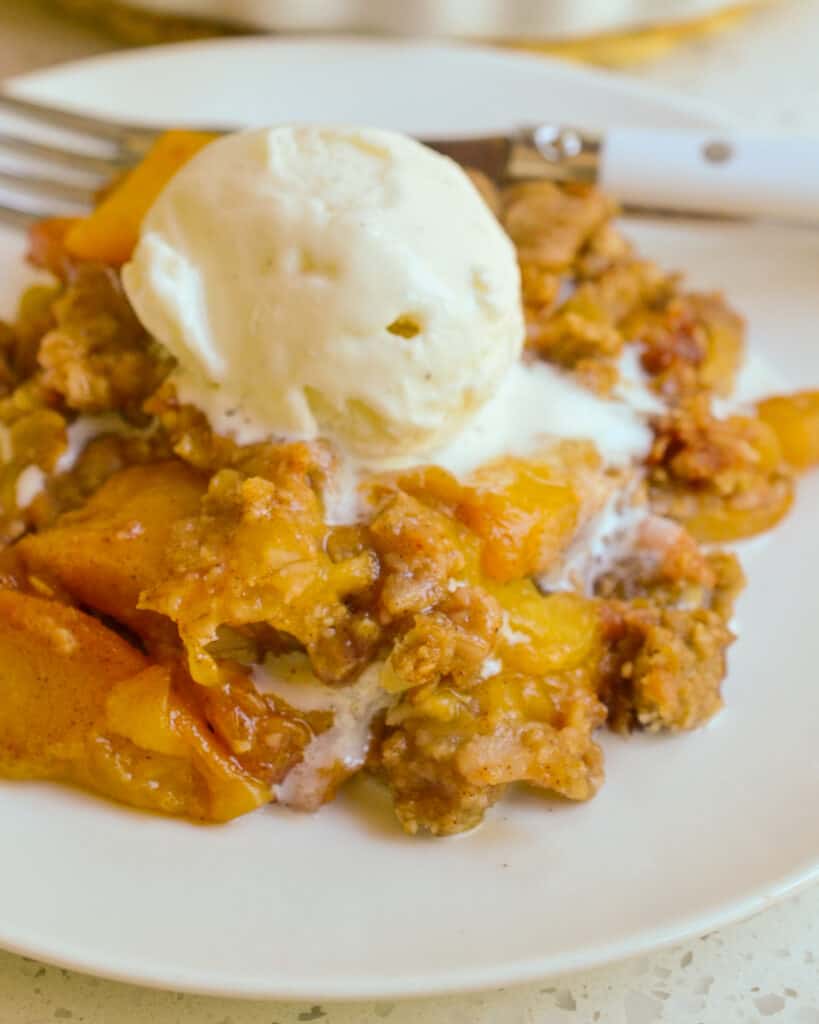 Peach crisp on a plate with juicy peaches soaked in a sweet cinnamon syrup and topped with a crispy crumble topping. 