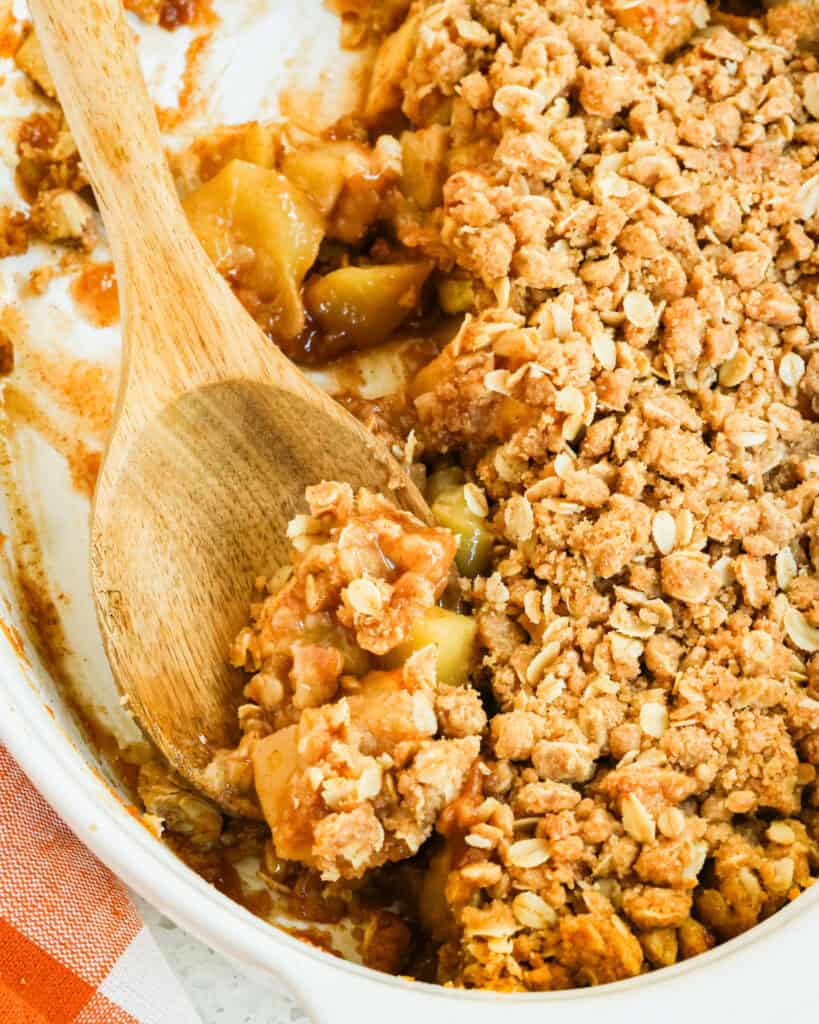 Apple crumble in a casserole dish with a wooden spoon full of apple crumble.