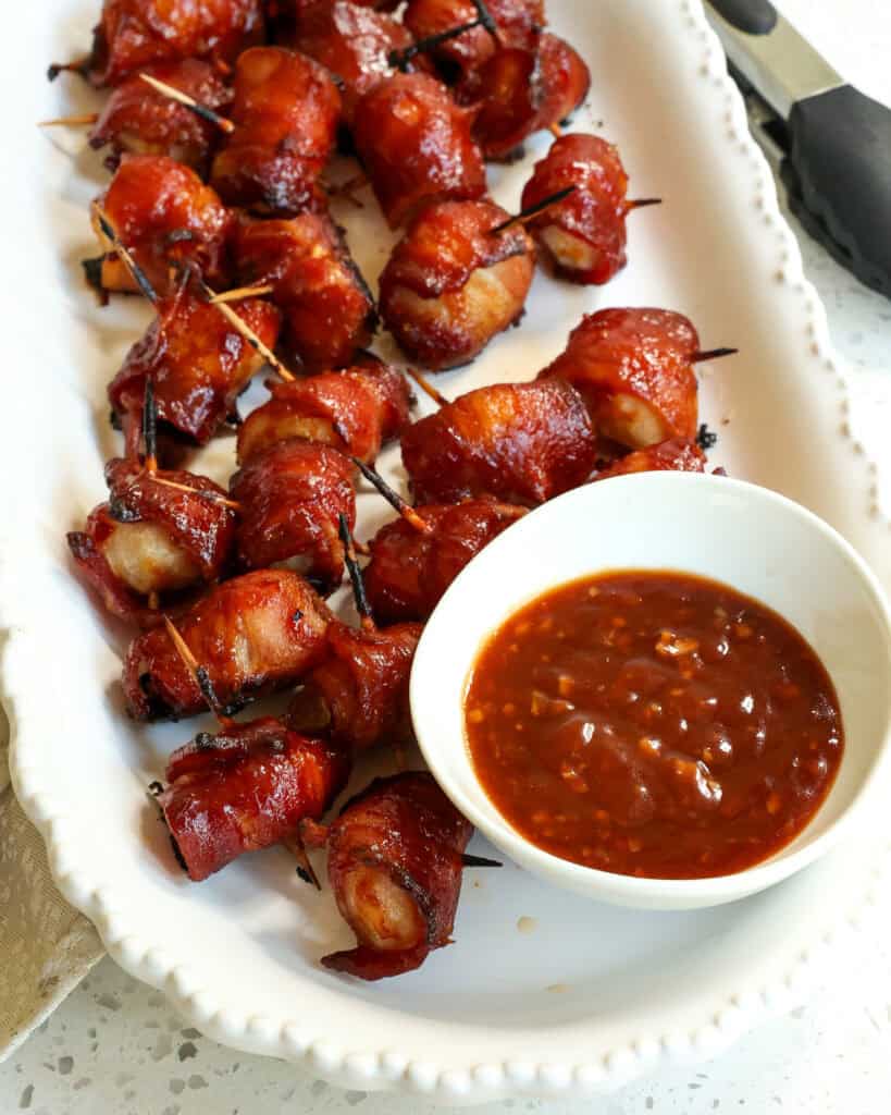Bacon Wrapped Water Chestnuts on a long white platter with the sauce.