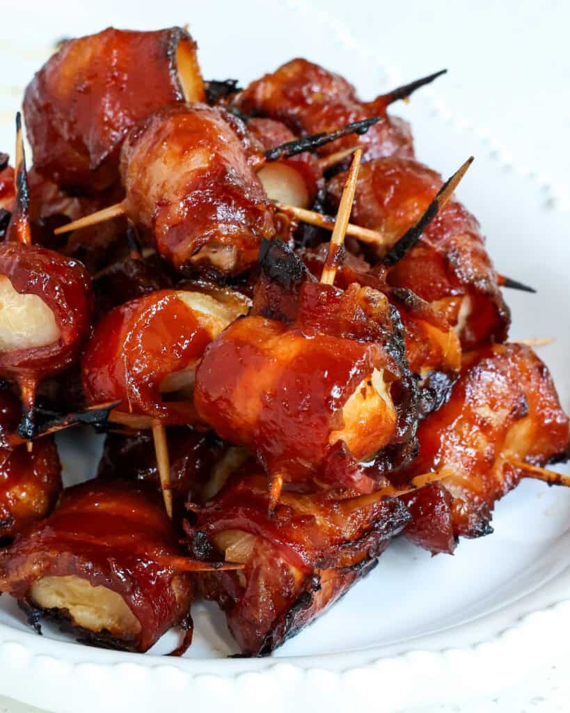 An up close view of Bacon Wrapped Water Chestnuts stacked on top of each other on a white platter.