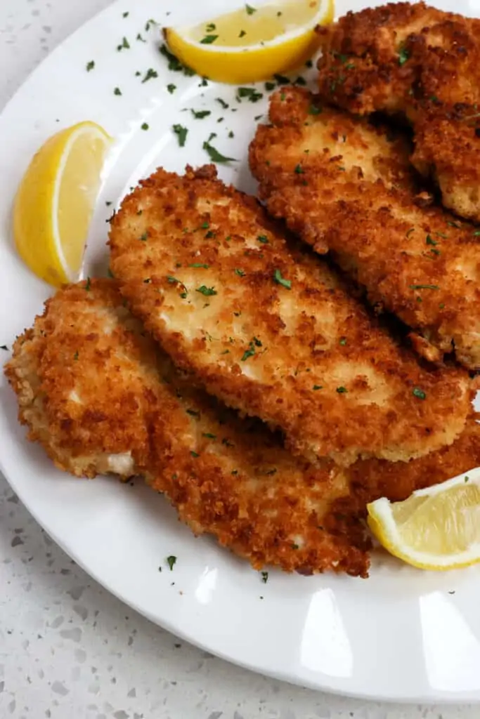 This Chicken Schnitzel recipe is breaded chicken cutlets pan fried to golden crispy perfection and served with lemon wedges and chopped fresh parsley.