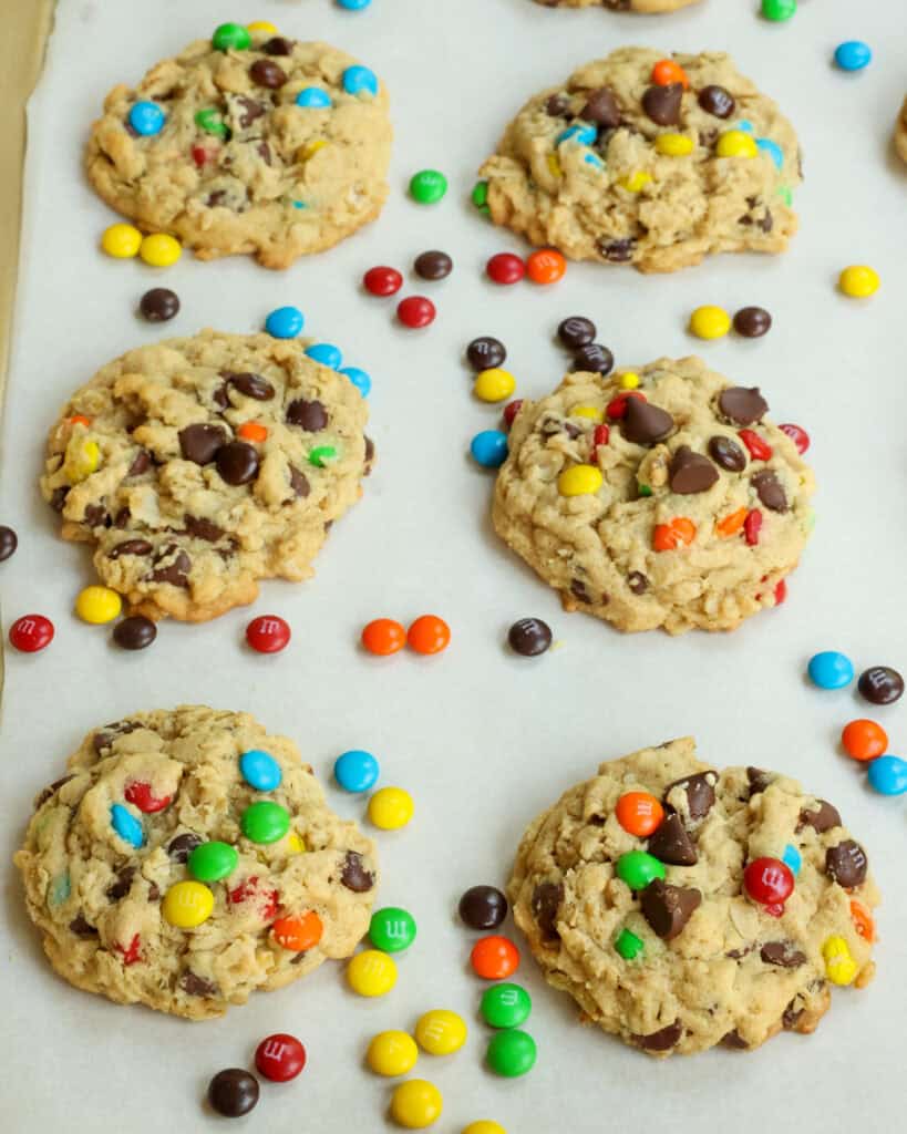 Monster cookies and mini M&Ms on a baking sheet covered with parchment paper. 