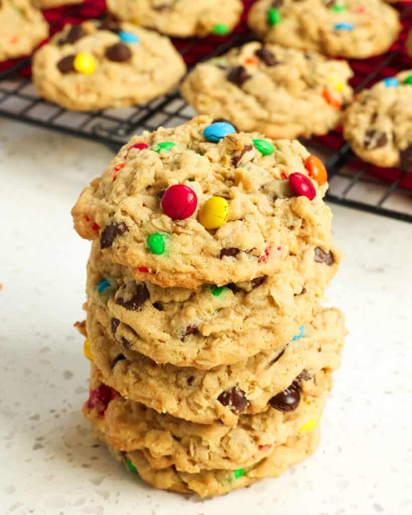 A stack of monster cookies in front of a cooling rack full of monster cookies. 