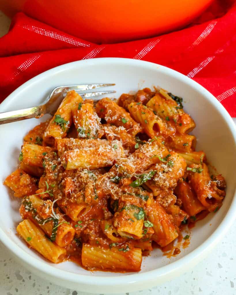 Pasta Bolognese in a bowl topped with basil and Parmesan cheese.