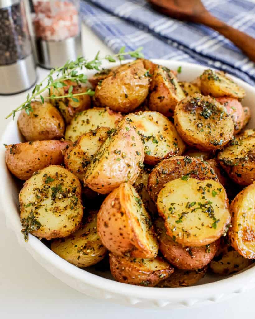 A close up view of roasted red potates with fresh thyme in a white serving bowl. 